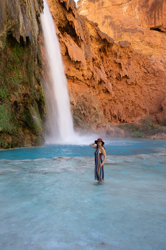 Agnes Stabinska, the author, stands in the blue water of Havasu Falls. Large streams of water flow from the orange wall.