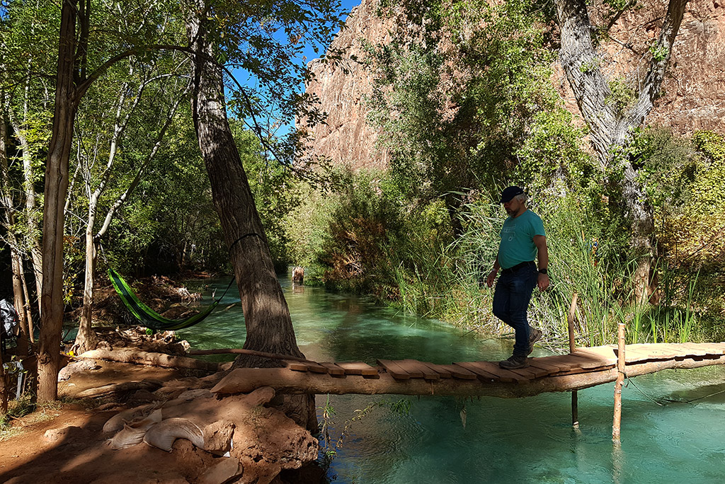 Chris, Agnes’s partner, crossing Havasu Creek on a wooden path, wearing hiking shoes.