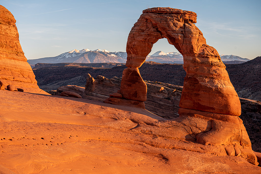 Delicate Arch after sunset with the mountains in the backdrop.