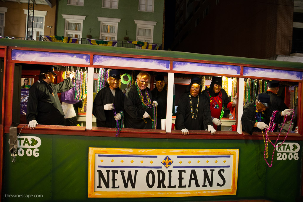 New Orleans Mardi Gras tram: inside, men in black cloaks and druidic masks with colorful beads in their hands.
