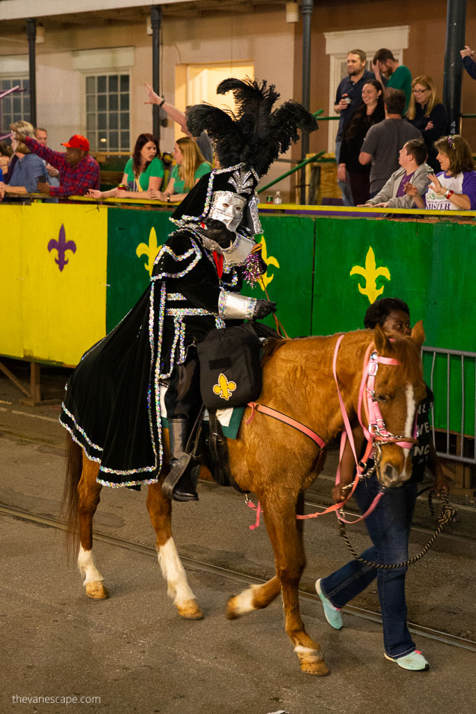 Men wearing masks and black costumes are on the horse on New Orleans streets during Mardi Gras parade.