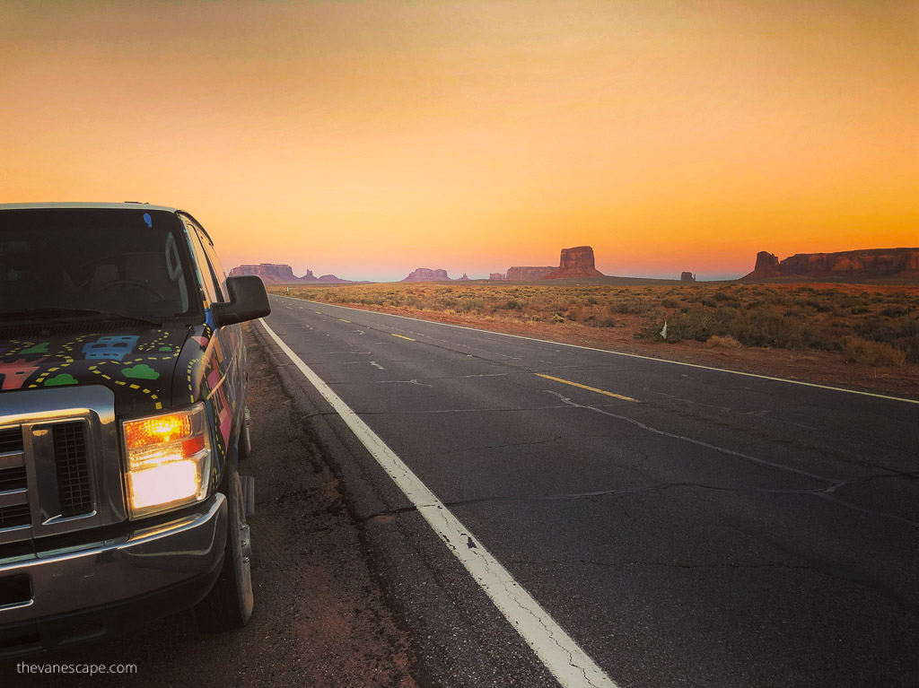 our rented van on the road during sunset with rock formations in Monument Valley in the backdrop.