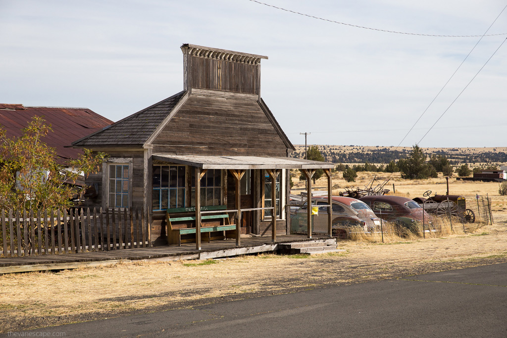 wooden old buildlings in Shaniko and old rusty cars along the road.