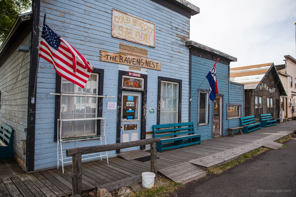 Old blue wooden building with a flying American flag and a sign on the building: Gold Nuget Saloon and The Raven Nest.