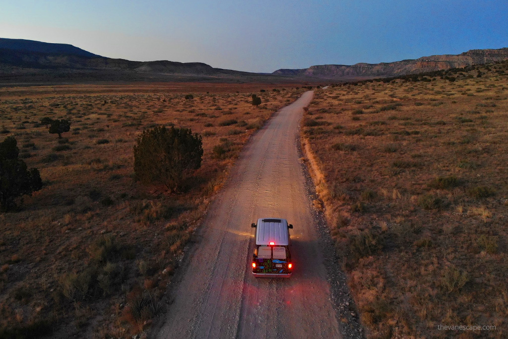 Our van on a gravel road among desert scenery after sunset.