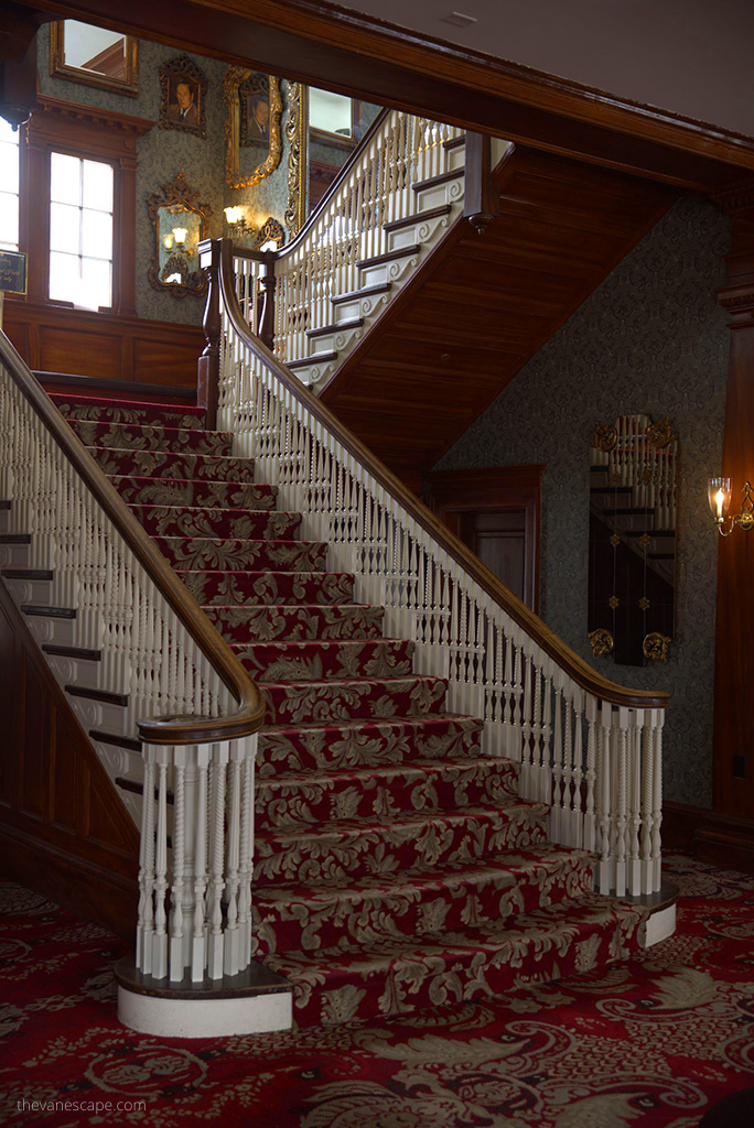 Antique stairs with beautiful decorative carpets, wooden handrail and paintings hanging on the wall in Stanley Hotel.