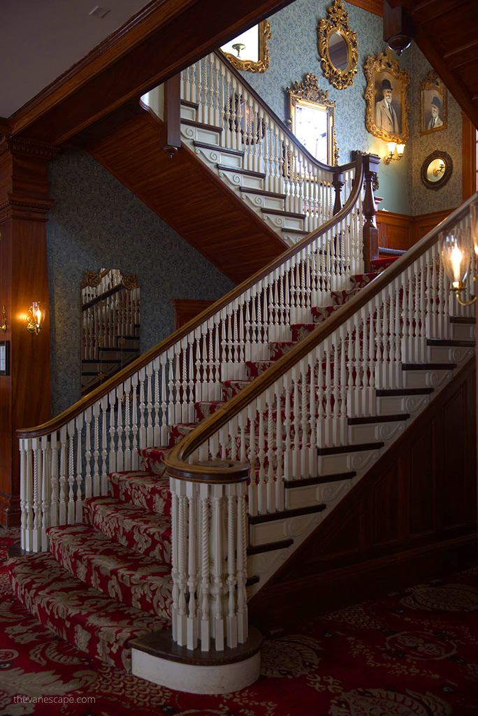 Antique stairs with beautiful decorative carpets, wooden handrail and paintings hanging on the wall in Stanley Hotel.
