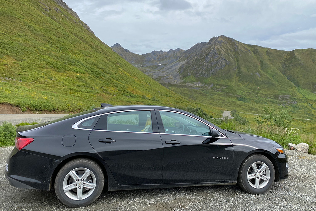 black rented malibu car among mountain scenery.