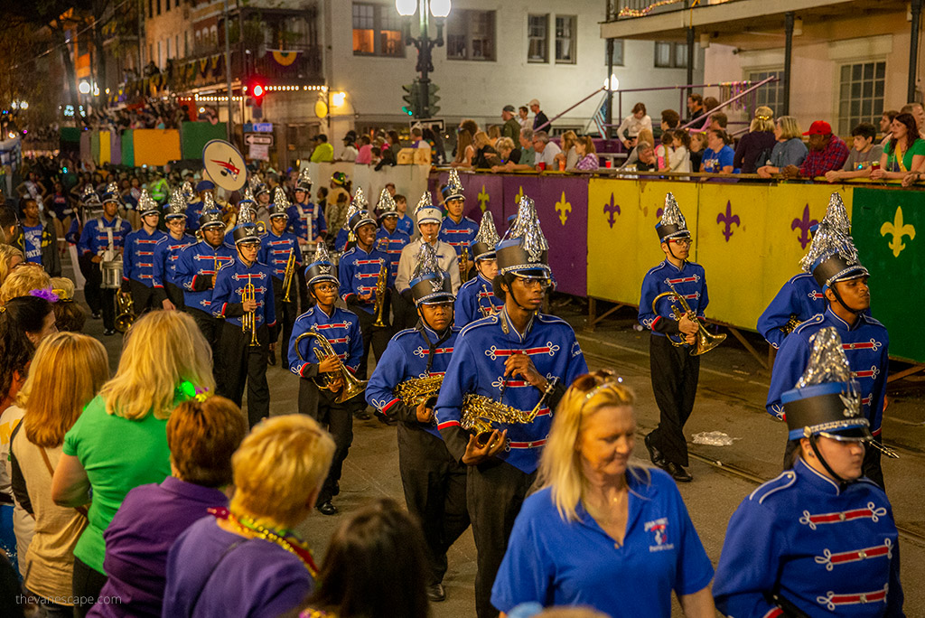 A youth marching band marches through the streets of new orleans, crowds of people cheering.
