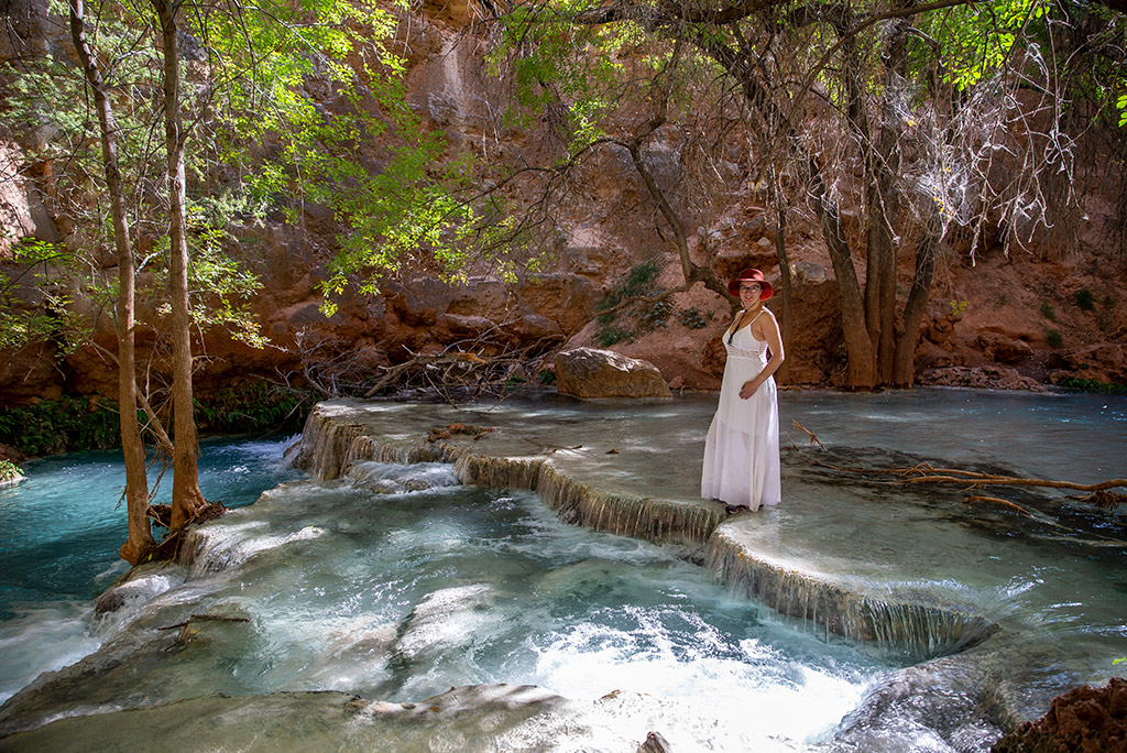 Agnes Stabinska, the author, stands barefoot in the water at Havasu Falls Campground, wearing a white dress and sun hat.