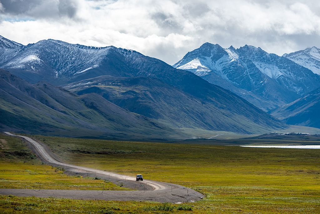Car on a gravel road with alaska mountains in the backdrop.