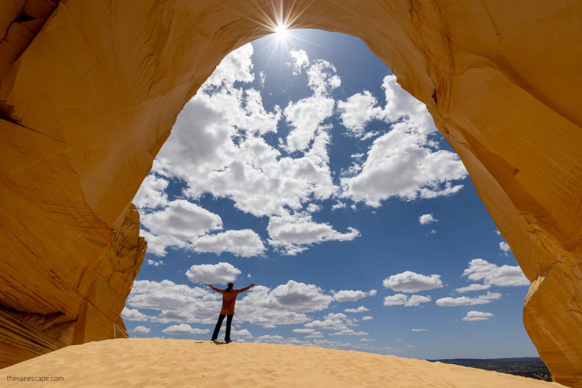 Agnes Stabinska, the author, in Great Chamber aka Cutler Cove in Kanab. She is standing on sandy dunes, the walls of chamber are yellow, the sun is on the blue skay.