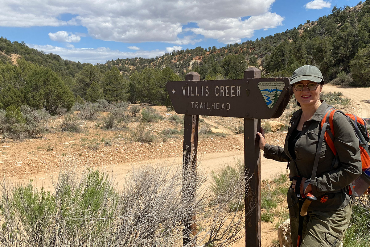 Agnes Stabinska, the author and co-owner of the best USA road trips blog, with the wooden sign which is pointed the beginning of the Willis Creek Trailhead
