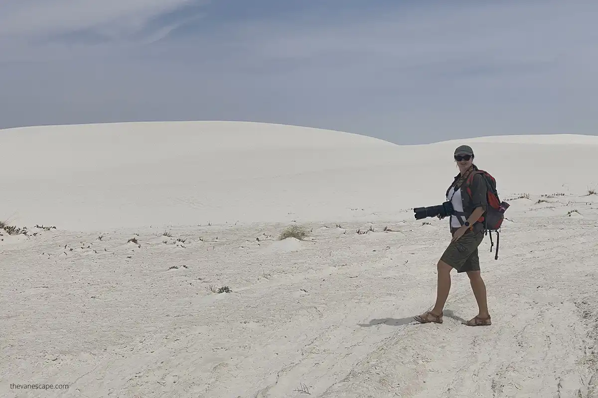 Agnes Stabinska, the author, is hiking in White Sand Dunes National Park wearing her backpack and camera with white dunes in the backdrop.